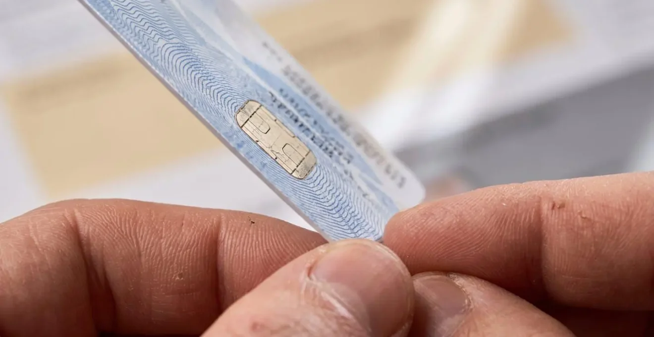 Mains tenant une carte Vitale avec documents administratifs flous en arrière-plan