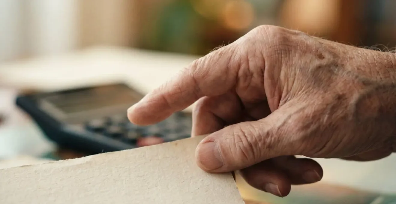 Main d'une personne âgée tenant une facture médicale avec une calculatrice floue en arrière-plan, symbolisant le calcul du reste à charge.